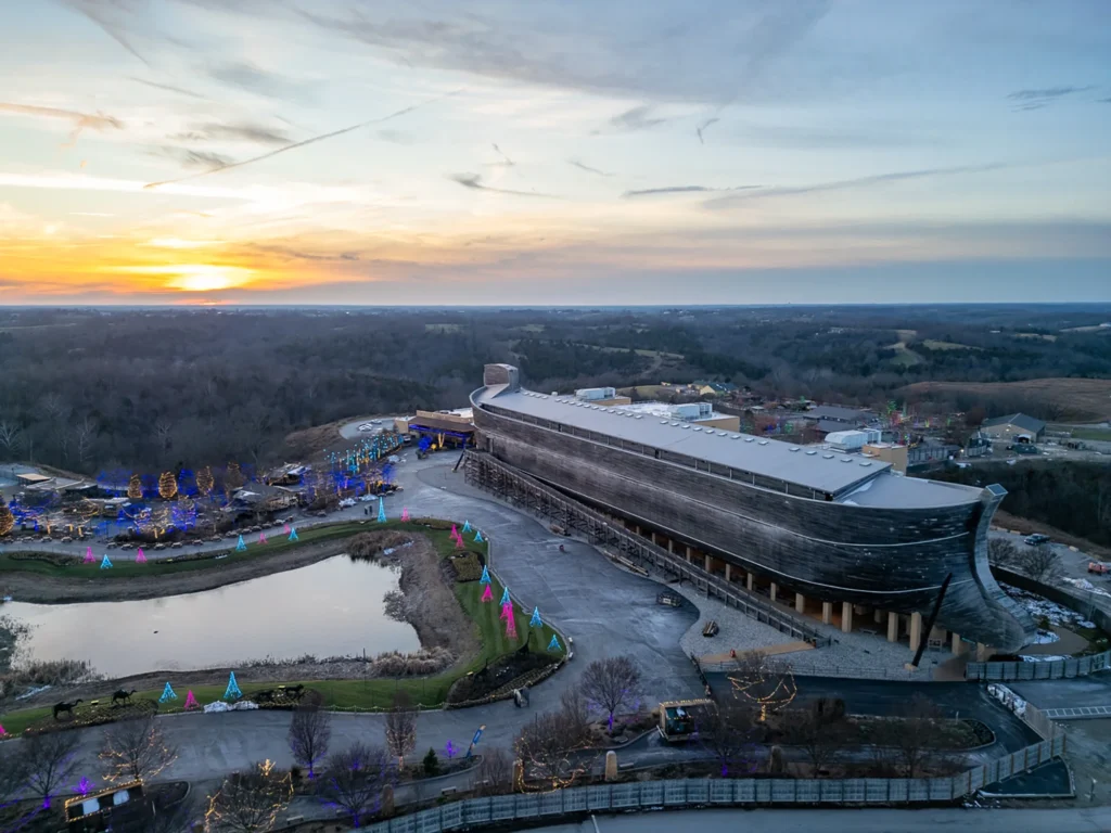 Aerial view of the Ark Encounter at sunset, featuring the massive wooden ark structure and a surrounding pond.