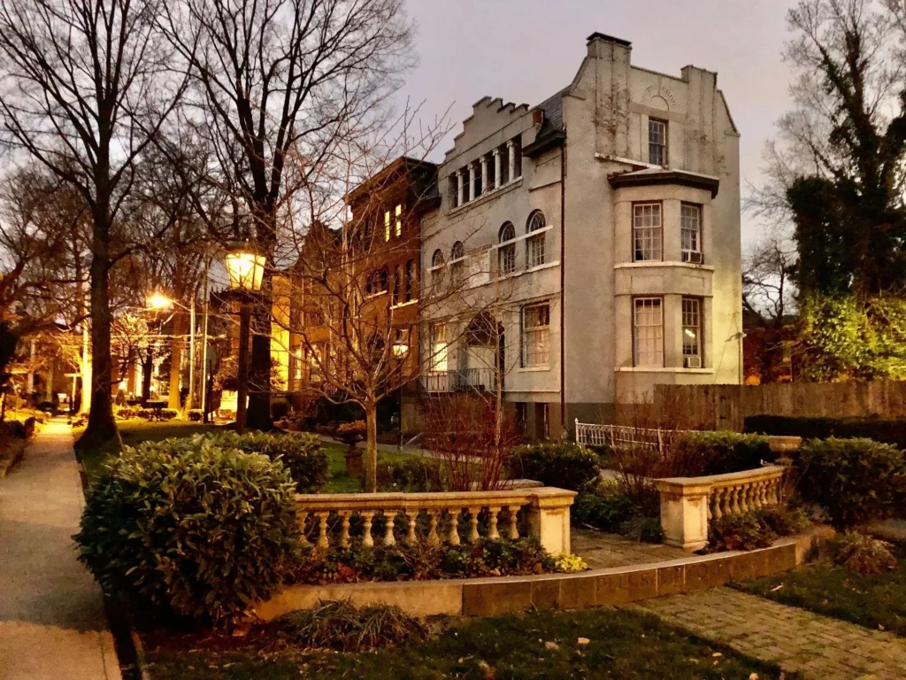 A stone mansion, brick building, and park-like front yard with a balustrade at dusk.