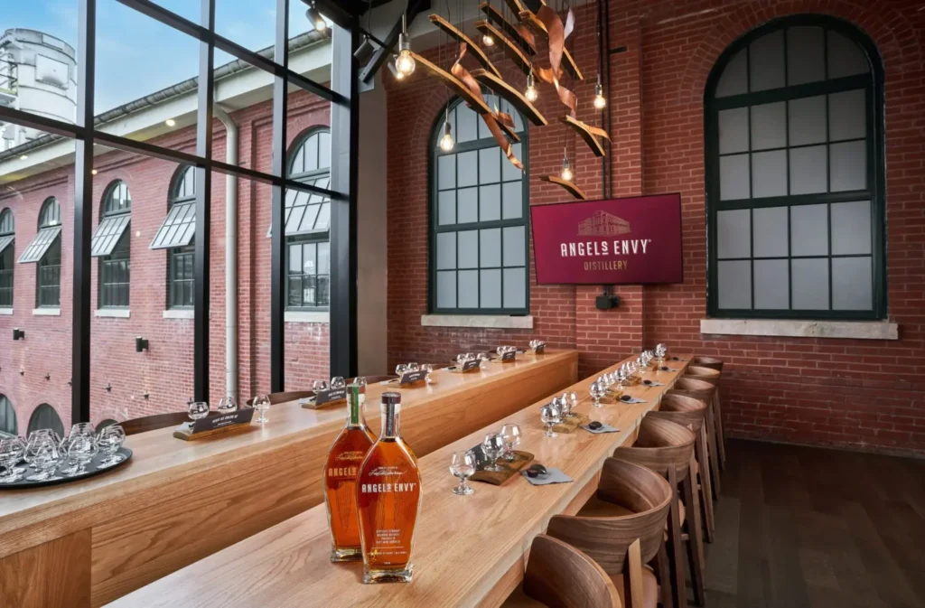 An Angel's Envy tasting room featuring wooden bars, bottles of bourbon, and large industrial-style windows.