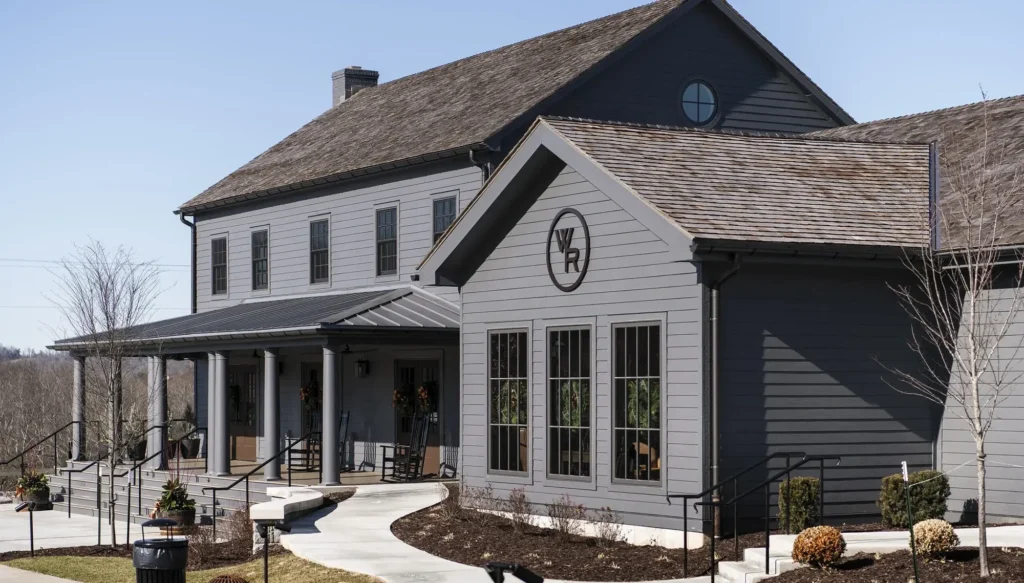 A two-story grey building with a covered porch, wood-shingled roof, and a circular "WR" logo on the front gable.