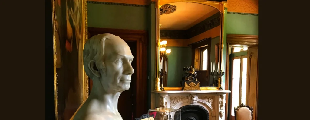 A white marble bust of a man is in the foreground, with a reflection of an ornate room visible in a large mirror.